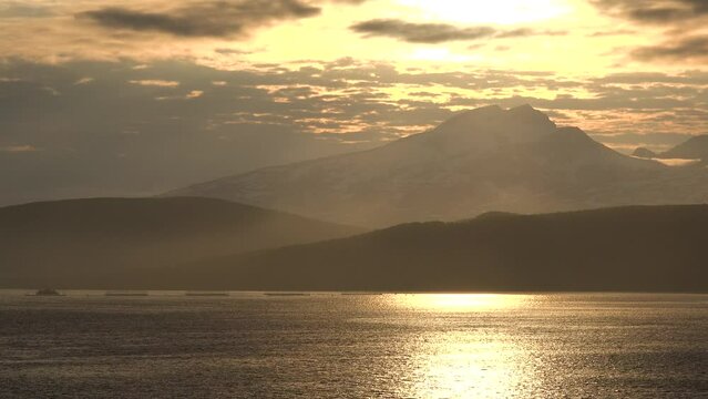 Sunrise or sunset at sea from sundeck of cruise ship. Morning sun, sunbeams and lens flare reflecting on sea surface with calm waves. On the horizon the coast of Norway. Voyage cruise travel concept