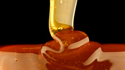 Golden Thick Honey Dripping close up. Pouring honey isolated on black background