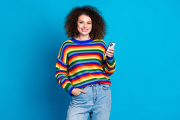 Photo portrait of lovely young lady hold device cheerful smile dressed stylish rainbow print garment isolated on blue color background