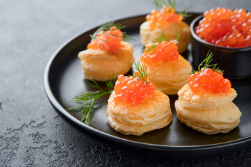 Salmon red caviar toast. Christmas canape or toast with red caviar on black plate on dark background. Idea to xmas snack. Gourmet food. Texture of caviar. Seafood.