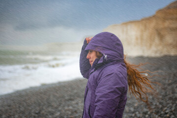 Women standing on a beach in the rain wearing a hood and looking out to sea