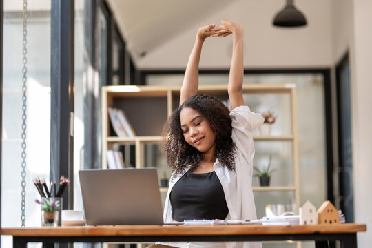 Black businesswoman stretching lazy at the desk to relax while working in the office. Feeling stressed and achy from work.