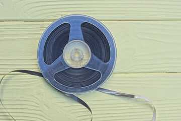 one old plastic black gray magnetic reel for a tape recorder lies on a yellow wooden table