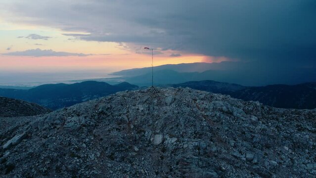 Broken torn wind sock on mountain top at sunset. Stormy dangerous bad weather. Rain clouds and hurricane in the distance
