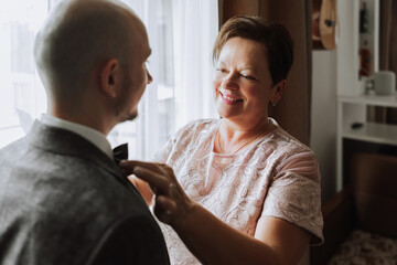 mother helps her adult son prepare for the wedding ceremony. An emotional and touching moment at a wedding. A mother hugs her son