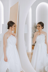 Naklejka premium Portrait of the bride in the hotel room. A beautiful young girl is dressed in a white wedding dress. Modern wedding hairstyle. Natural makeup.