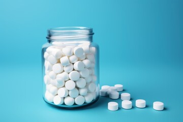 White pills in a glass jar on blue background. Focus on foreground. The concept of pharmacology, maintaining health with pills and supplements