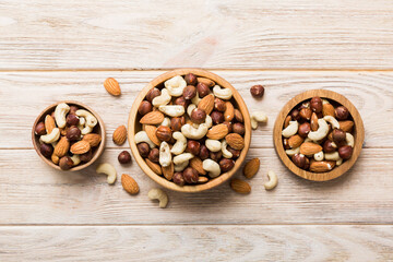 Assortment of nuts in wooden bowl on colored table. Cashew, hazelnuts, walnuts, almonds. Mix of nuts Top view with copy space