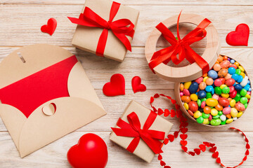 Red envelope with candy and gift box and Valentines hearts on colored background. Flat lay, top view. Romantic love letter for Holiday concept