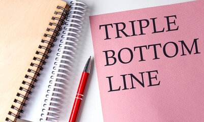 TRIPLE BOTTOM LINE word on the pink paper with office tools on white background