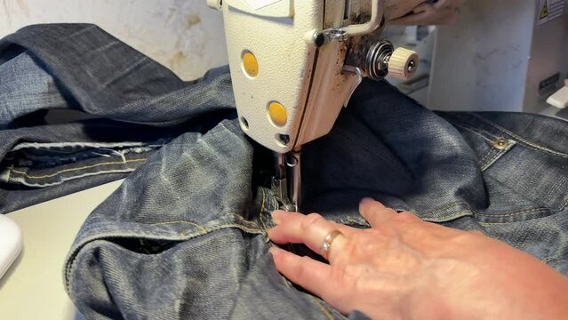 Untitled Sewing work. Stitching a hole in jeans with a sewing machine. Seamstress sews with jeans cloth. Darning jeans on a sewing machine. Seamstress sews on a sewing machine. Tailoring.