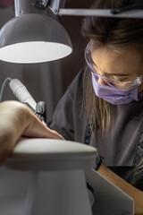 Manicurist at work. Professional manicurist removes old worn nail design from nails of client using modern electric drill. Preparing fingernails for making fresh manicure and applying new nail design