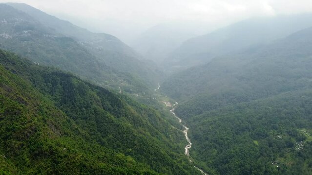Aerial, tilt down, drone shot, above the tista river, in a valley between mountains and Indian forest, on a sunny day, in sikkim, India