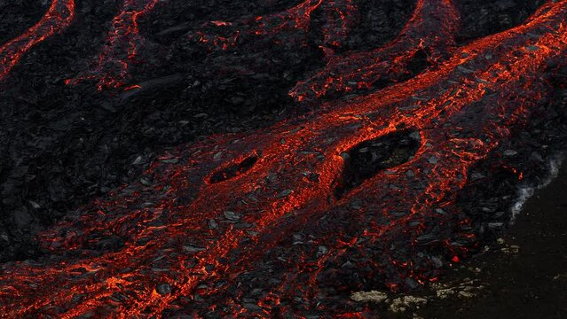 Unique view of molten lava flow burning and slowly moving down rugged volcanic rocks terrain, aerial close up shot. Volcano eruption and natural disaster concepts.