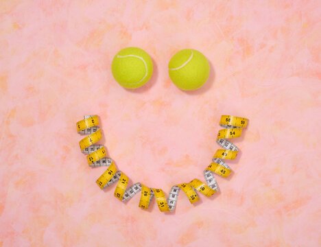 Two yellow tennis balls and a measuring tape in the shape of a smiley face. Fitness and workout wellness concept, top view.