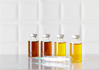 Group of glass bottles of injectable medicine and a syringe on white laboratory table. White background.
