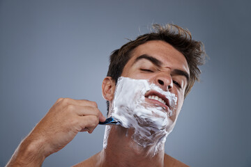 Man, shaving and stress with razor in studio portrait for wellness, skin and grooming by grey...