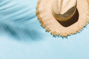 Summer flat lay with straw hat on blue background with palm leaf shadow, sun and sunlight....