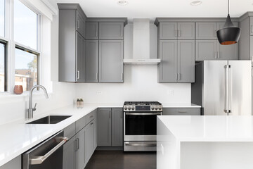 A kitchen detail with grey cabinets, white marble countertops and waterfall island, and stainless steel appliances. No brands or labels.