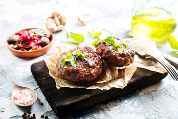 Tasty grilled hamburger patties with seasonings on wooden board