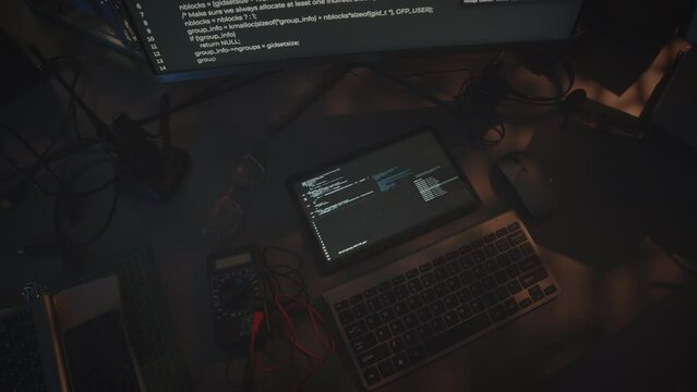 Top view of white html code running on black background at computer and digital tablet displays on desk at night military control department workplace