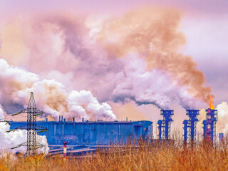The pipes of the a chemical plant, from which thick orange and white smoke rises into the sky. Air...