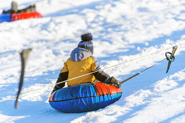 A little boy-child rides a tubing down a hill in the snow in winter. Winter entertainment. Snow fun. - obrazy, fototapety, plakaty