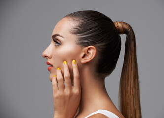 Manicure, face and profile of woman in makeup, beauty and cosmetics with nails and hair care on grey background. Hand, yellow nail polish and lipstick with skin, glamour and shiny ponytail in studio - obrazy, fototapety, plakaty