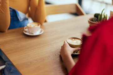 Close-up of the two cups of coffee on the table, females drinking cappuccino at the cafe.