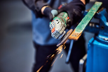 Close-up of a male holding and using a grinder to fix some metal parts, wearing protective gloves.