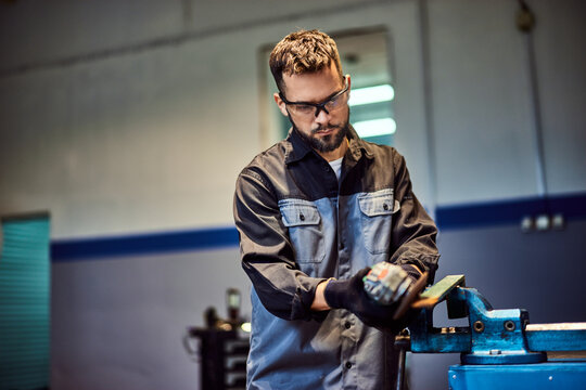 A hardworking man using a grinder, working at his repair shop, fixing some metal parts.