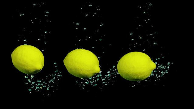 Three Lemons splash in water Slow motion. Close-up of falling ripe lemons and limes into sparkling water on black background,