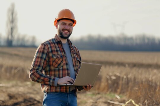 Happy engineer with laptop standing on field
