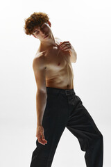Photo of athletic man, ballet dancer dressed in black trousers making dance elements against white...