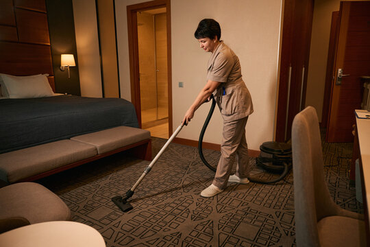 Uniformed chambermaid occupied with vacuuming guest suite