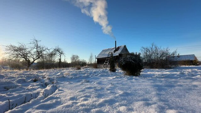 Bathhouse in village in winter time. Smoke from a bathhouse chimney in village. Russian Bath House in countryside. Wooden home in rural in winter. Smoke from Country houses chimney in countryside.