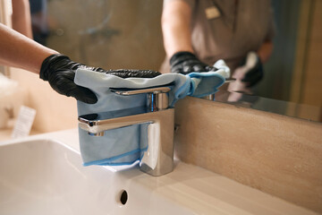 Female hand is cleaning water faucet in bathroom