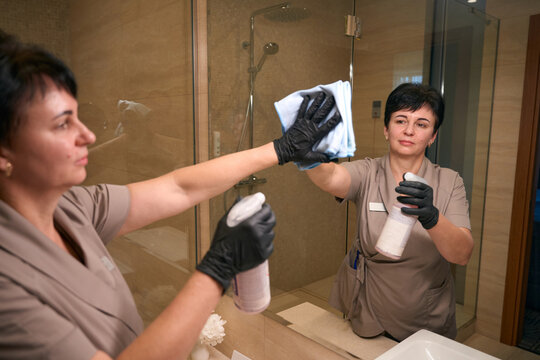 Uniformed chambermaid is cleaning hotel bathroom fixtures