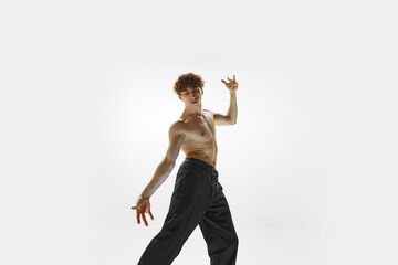 Young Caucasian man, ballet dancer performing against white studio background. Modern dance style....