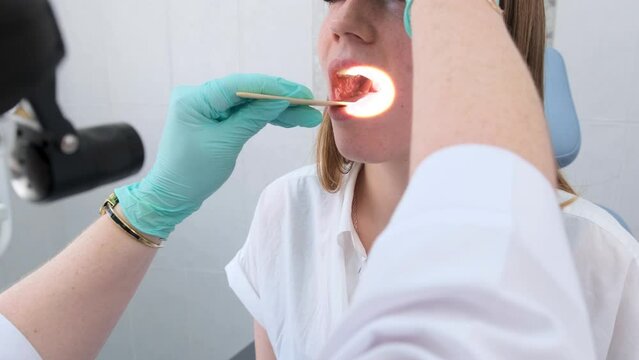 a female otolaryngologist examines the patient's oral cavity with a flashlight.