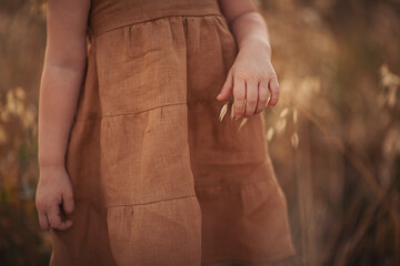 Little girl holding oat stems in evening light. Rural slow life. Girl in rustic linen dress...