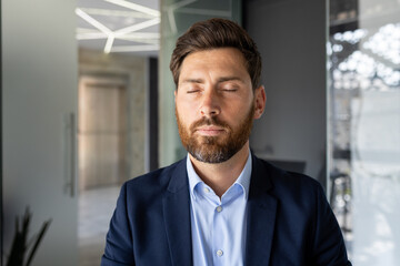 Fototapeta premium Close-up portrait of a young man working in the office, sitting thoughtfully in a suit with closed eyes and resting