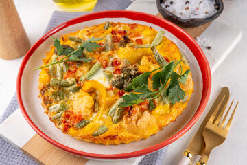 Homemade vegetable casserole frittata, healthy vegetarian food, frying pan or oven baked egg omelette with vegetables on white marble kitchen table copy space
