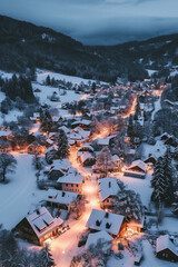 Drone photo of a snow-covered village, warm lights twinkling at dusk