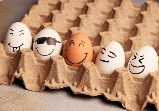 Photograph of white eggs with faces next to a brown egg.
