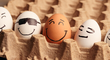 Photograph of white eggs with faces next to a brown egg. - obrazy, fototapety, plakaty