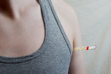 A patient wearing a gray shirt has a thermometer under his armpit in a close-up shot. High...