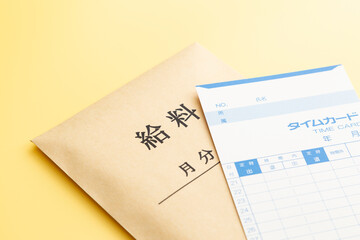 黄色背景にタイムカードと給料袋