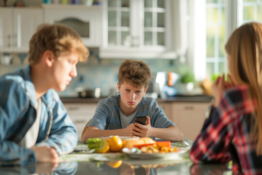 Teenage boy using mobile phone and his arguing parents at table in kitchen