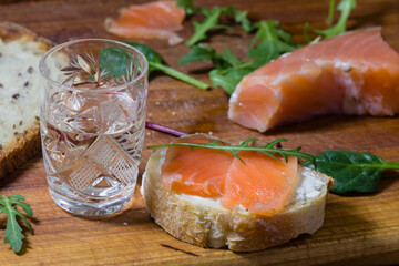 a glass of vodka and a sandwich with red fish